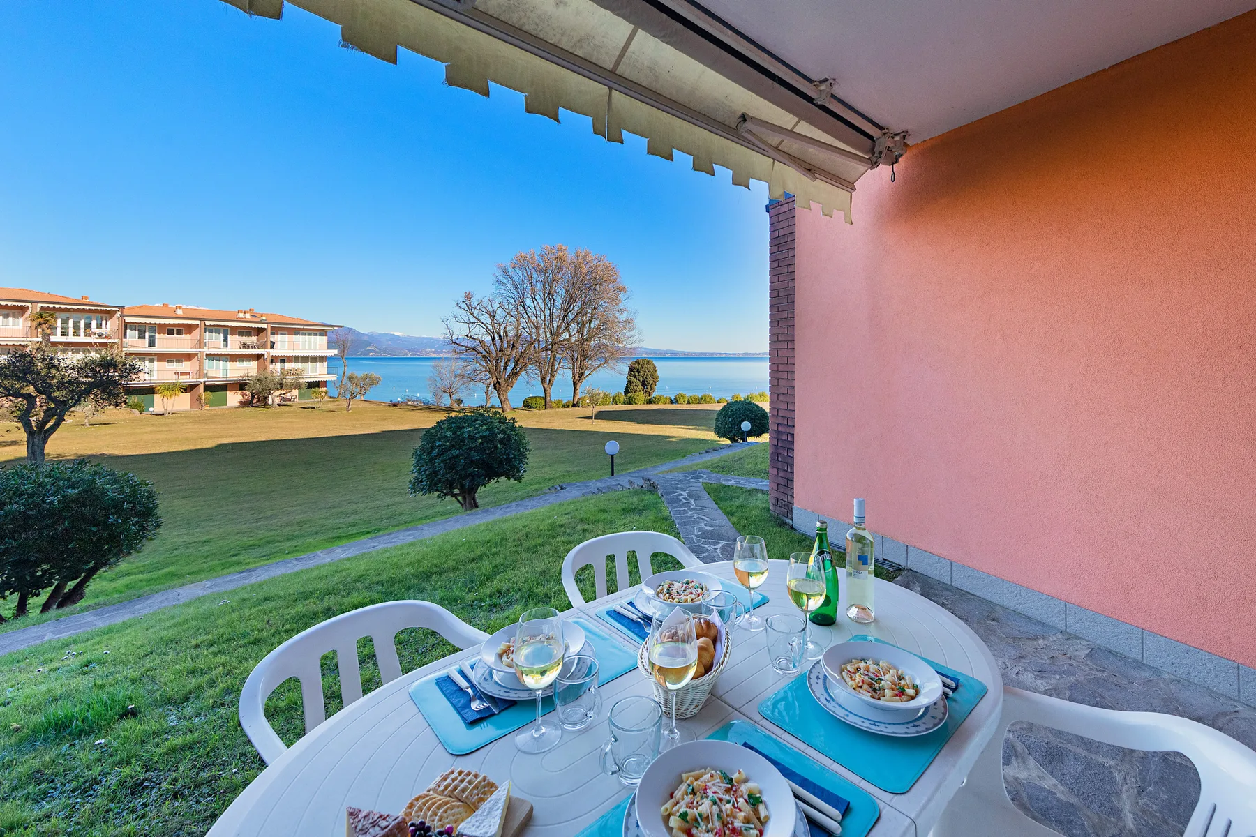 Una zona de comedor en un patio cubierto da a un césped, edificios cercanos y el agua.
