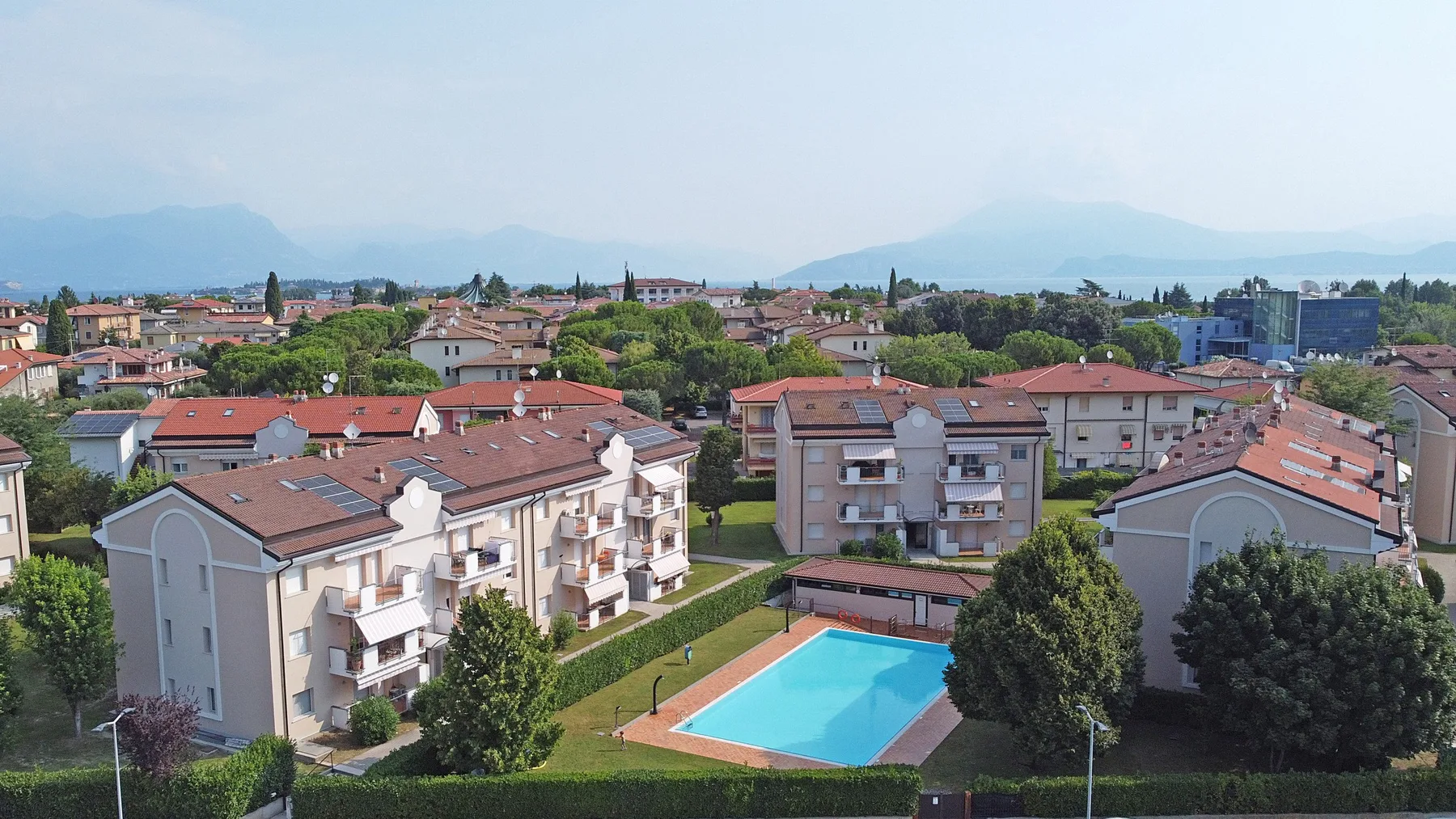 Un barrio residencial con una piscina exterior azul y montañas a lo lejos.