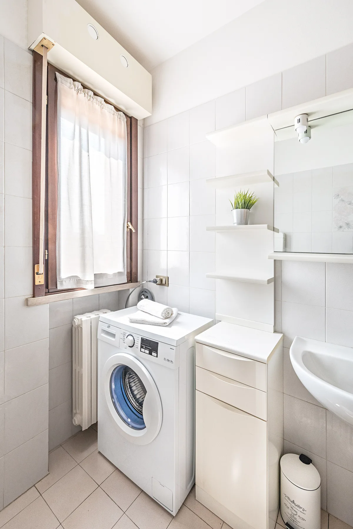 Un baño luminoso con una lavadora debajo de una ventana.
