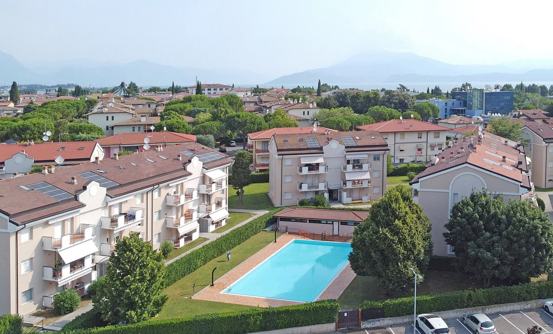 Edificios residenciales rodean una piscina al aire libre, con montañas a lo lejos.