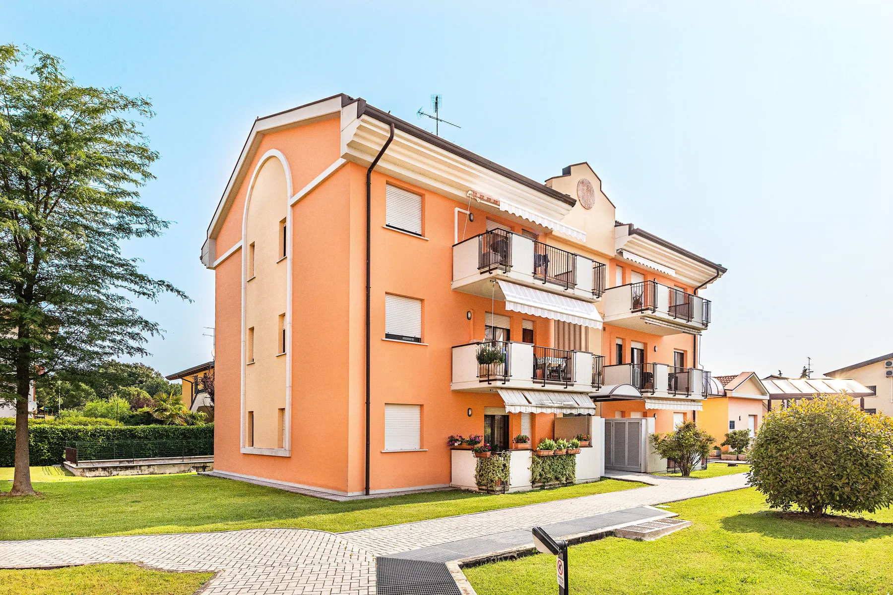 Un edificio residencial naranja de varias plantas se alza junto a un sendero pavimentado y césped verde.