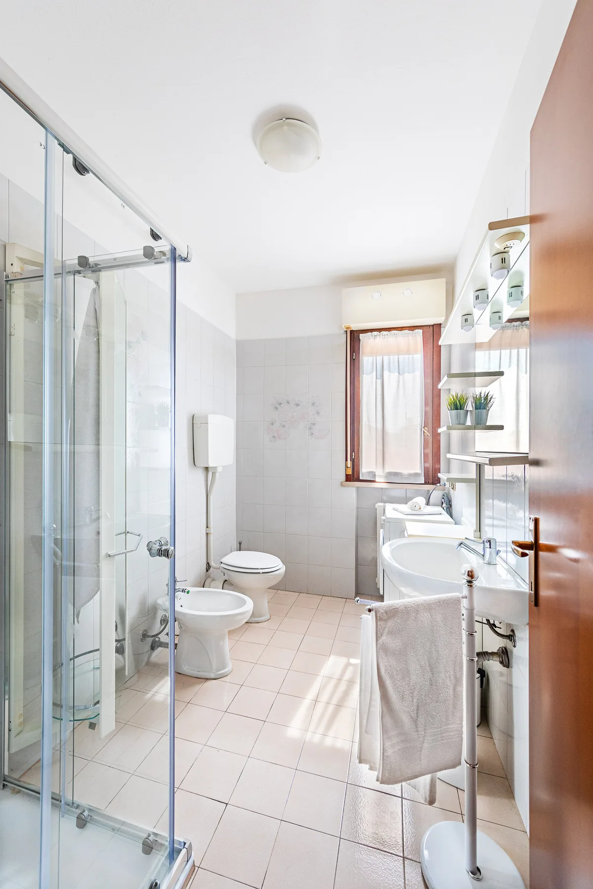 Un baño luminoso con una ducha de cristal y una ventana al fondo.
