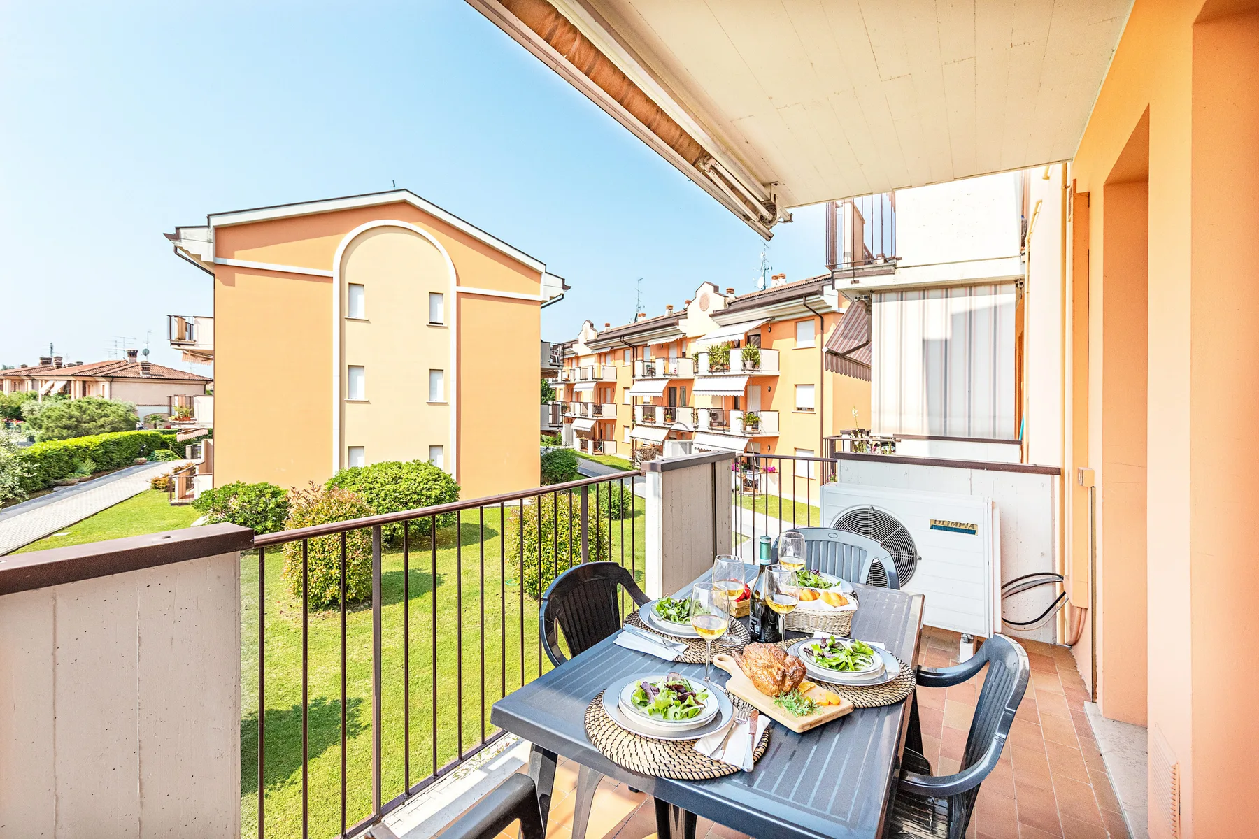 Una zona de comedor en el balcón da a edificios de apartamentos y vegetación.