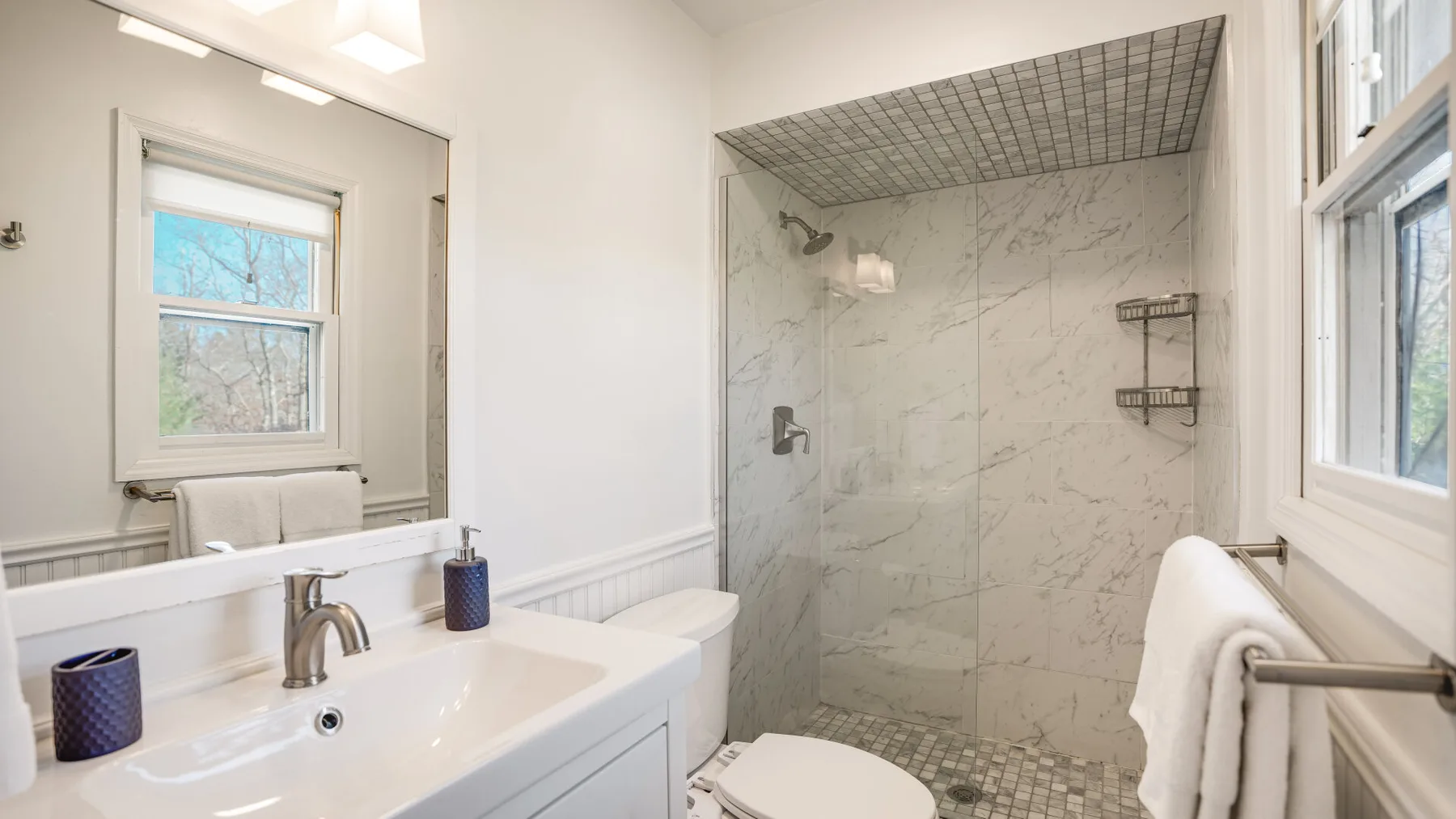 A bright bathroom with a sink, toilet, and glass-enclosed shower.