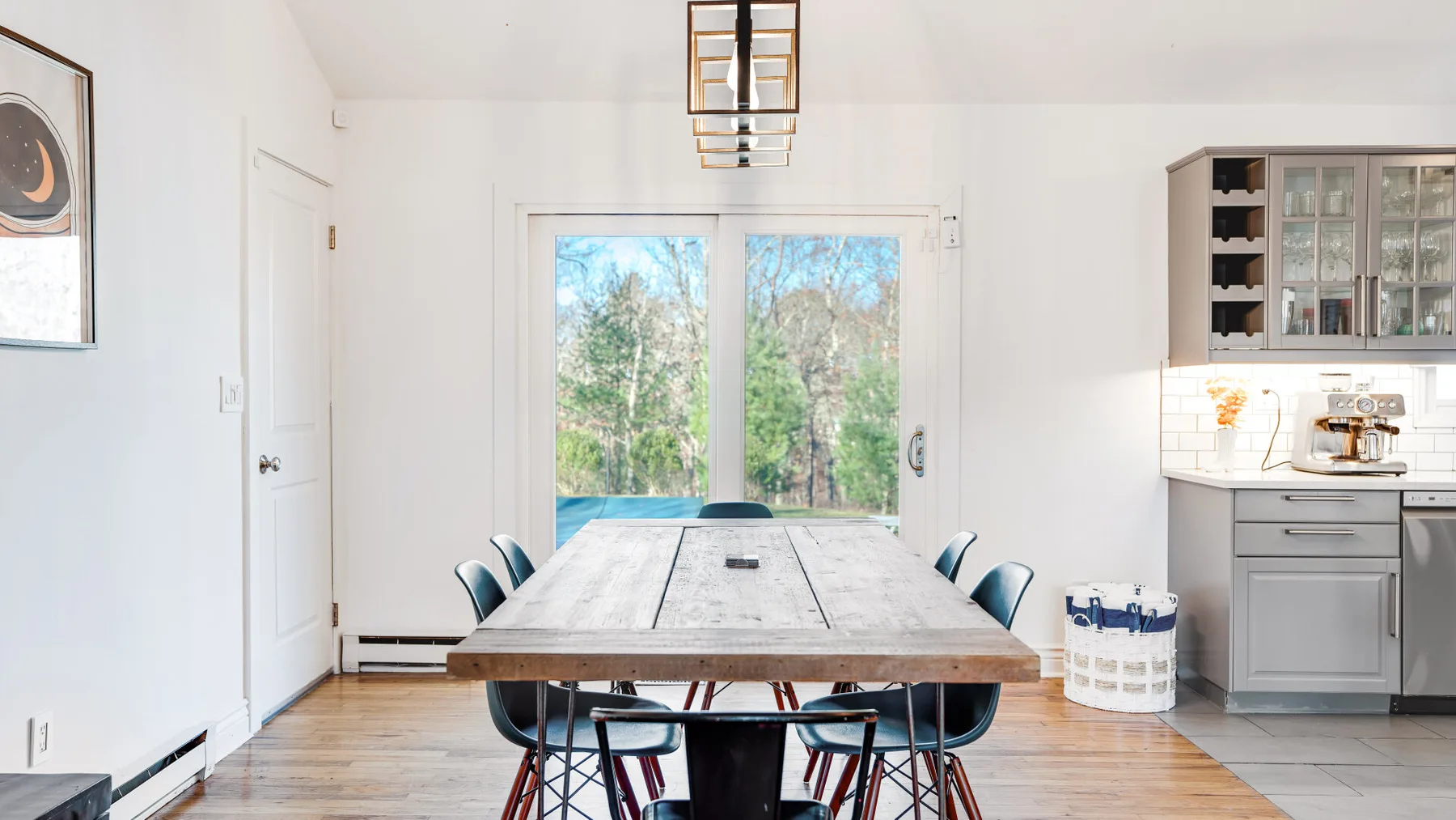 A dining area with a long table and chairs beside a bright kitchen.