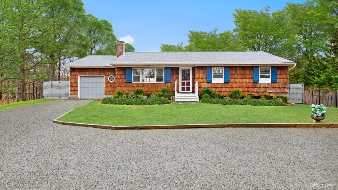 A single-story house with wood-shingle siding stands behind a gravel driveway.