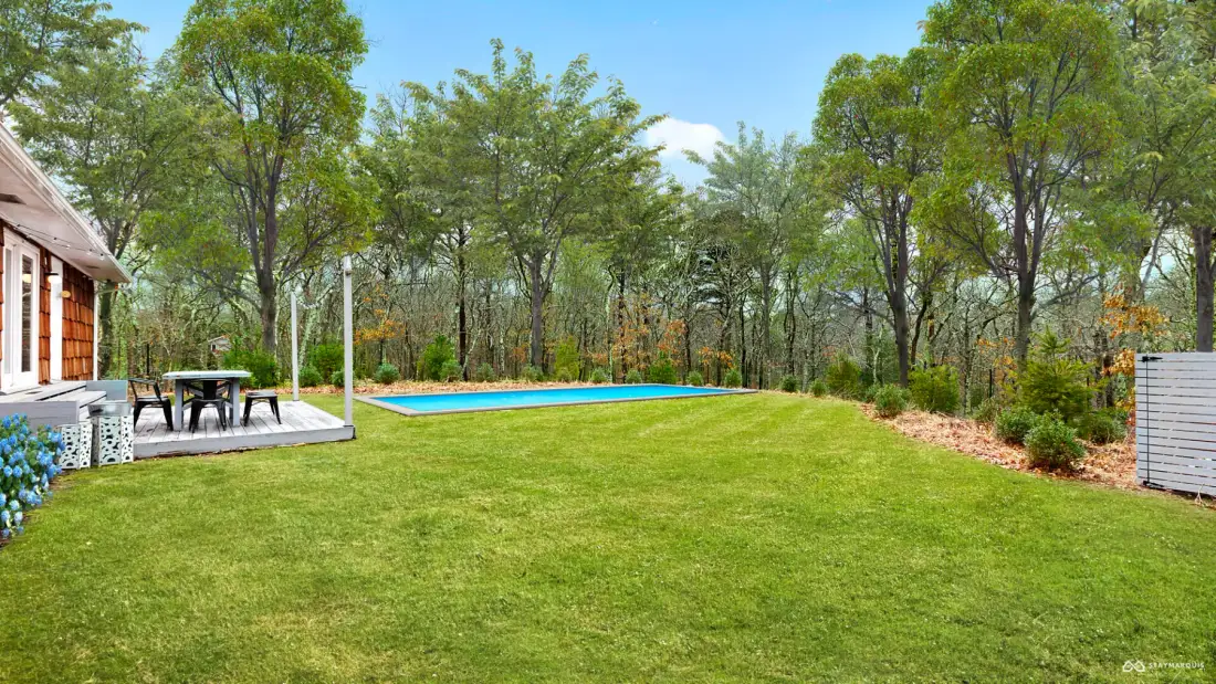 A grassy yard with a swimming pool, outdoor seating, and trees.