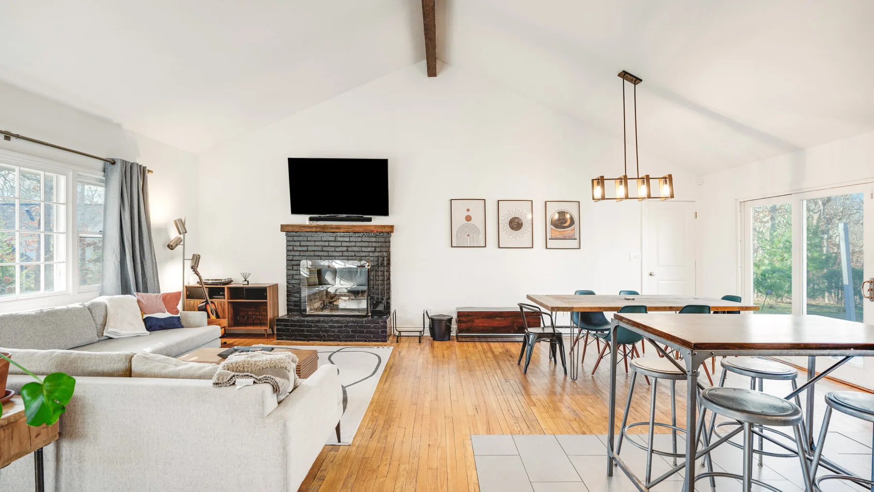 A bright living and dining area has a fireplace, seating, and a long table.