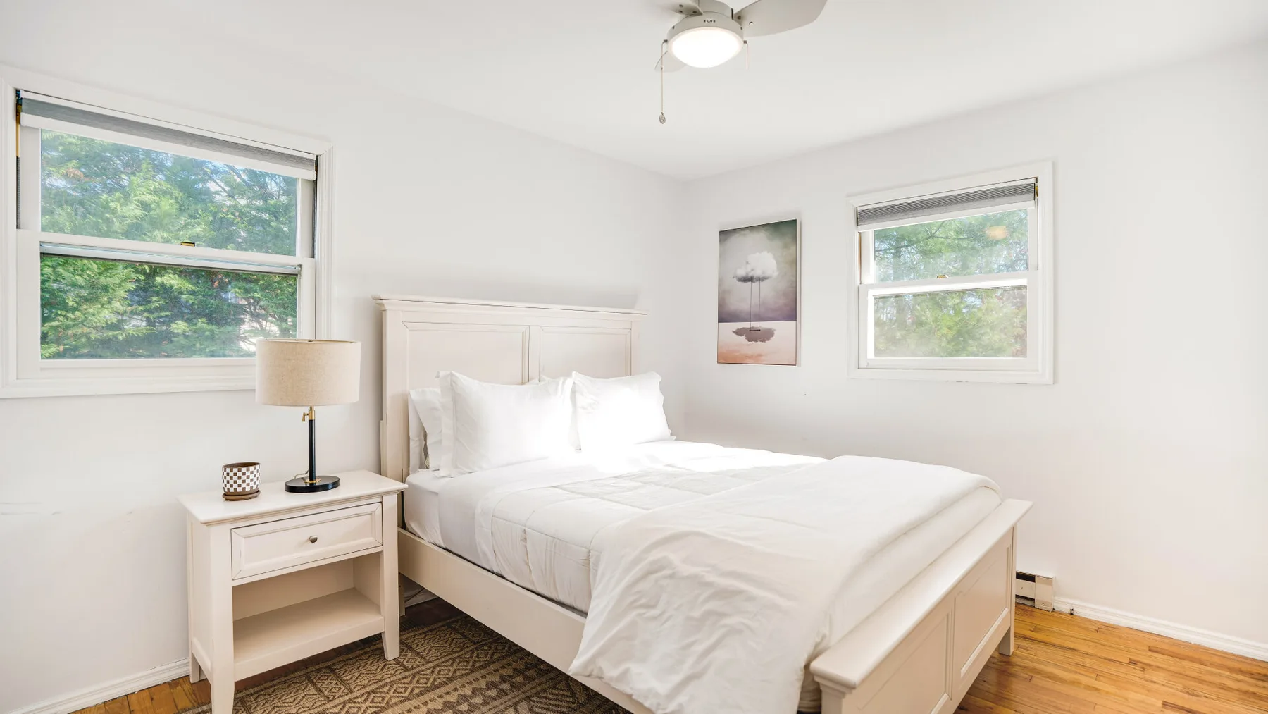 A bright bedroom with a bed, bedside table, and windows overlooking greenery.