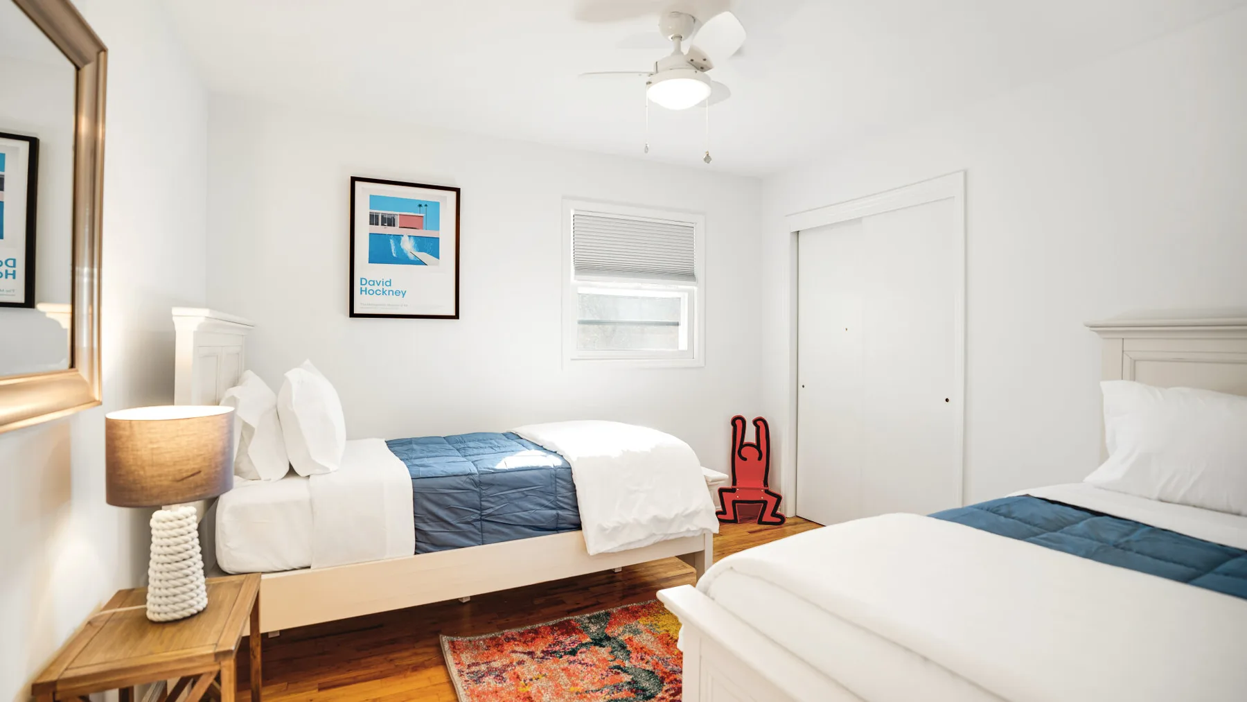 A bright bedroom with two beds, white bedding, and blue bedspreads.