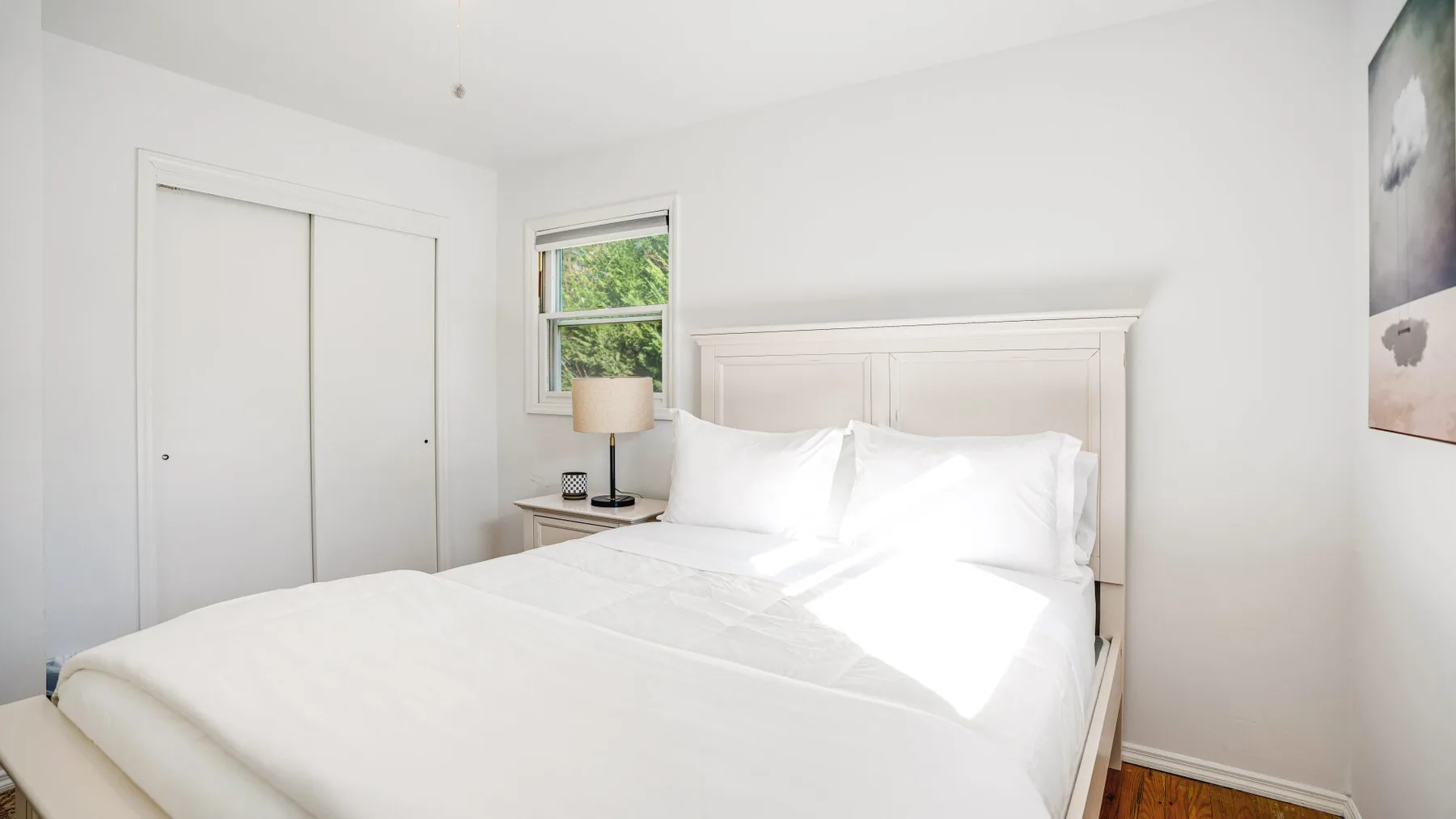 A bright bedroom with a white bed beside a window.