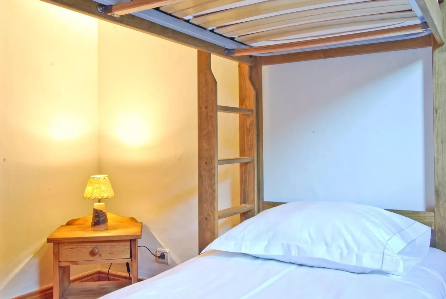 A bedroom with a wooden bunk bed, white bedding, and a bedside lamp.