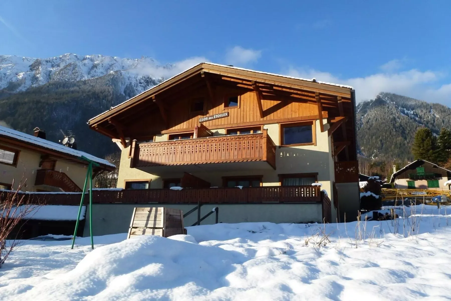 A wooden chalet stands in a snowy mountain setting beneath a clear blue sky.