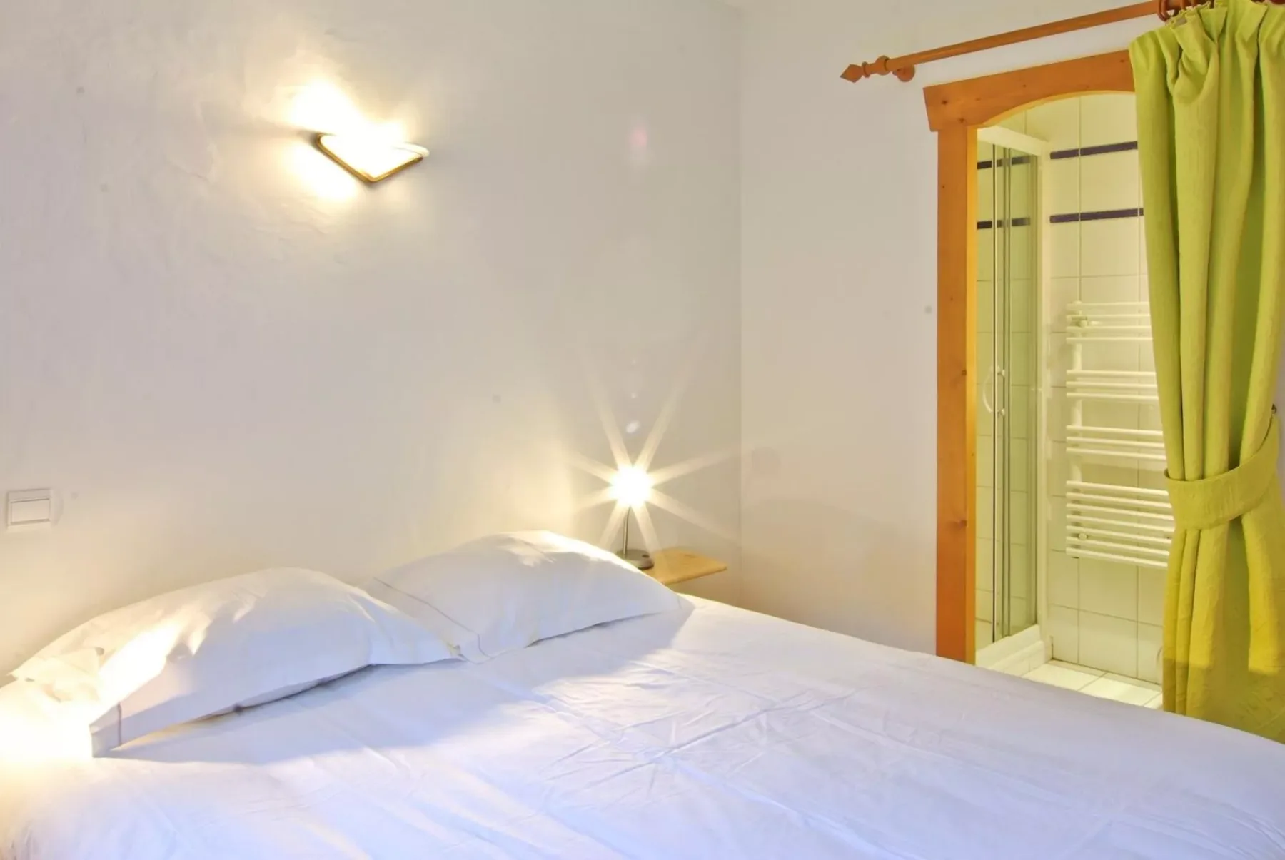 A bedroom with a bed beside a curtained shower area.