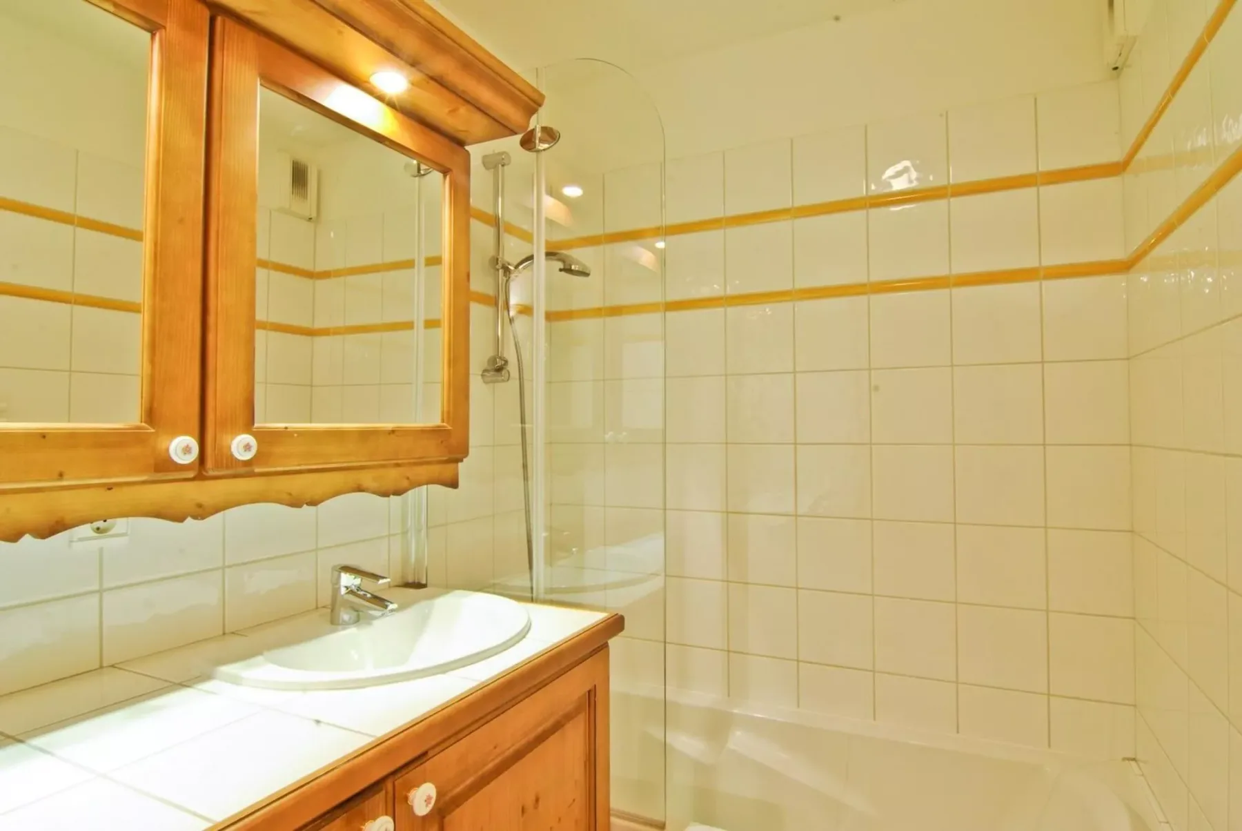 A tiled bathroom with a sink, wooden vanity, and shower.