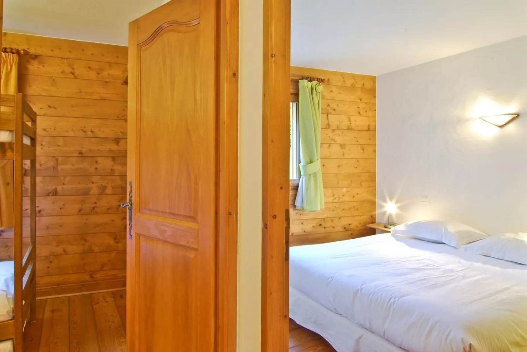 A bedroom with a bed, wood-paneled walls, and an open wooden door.