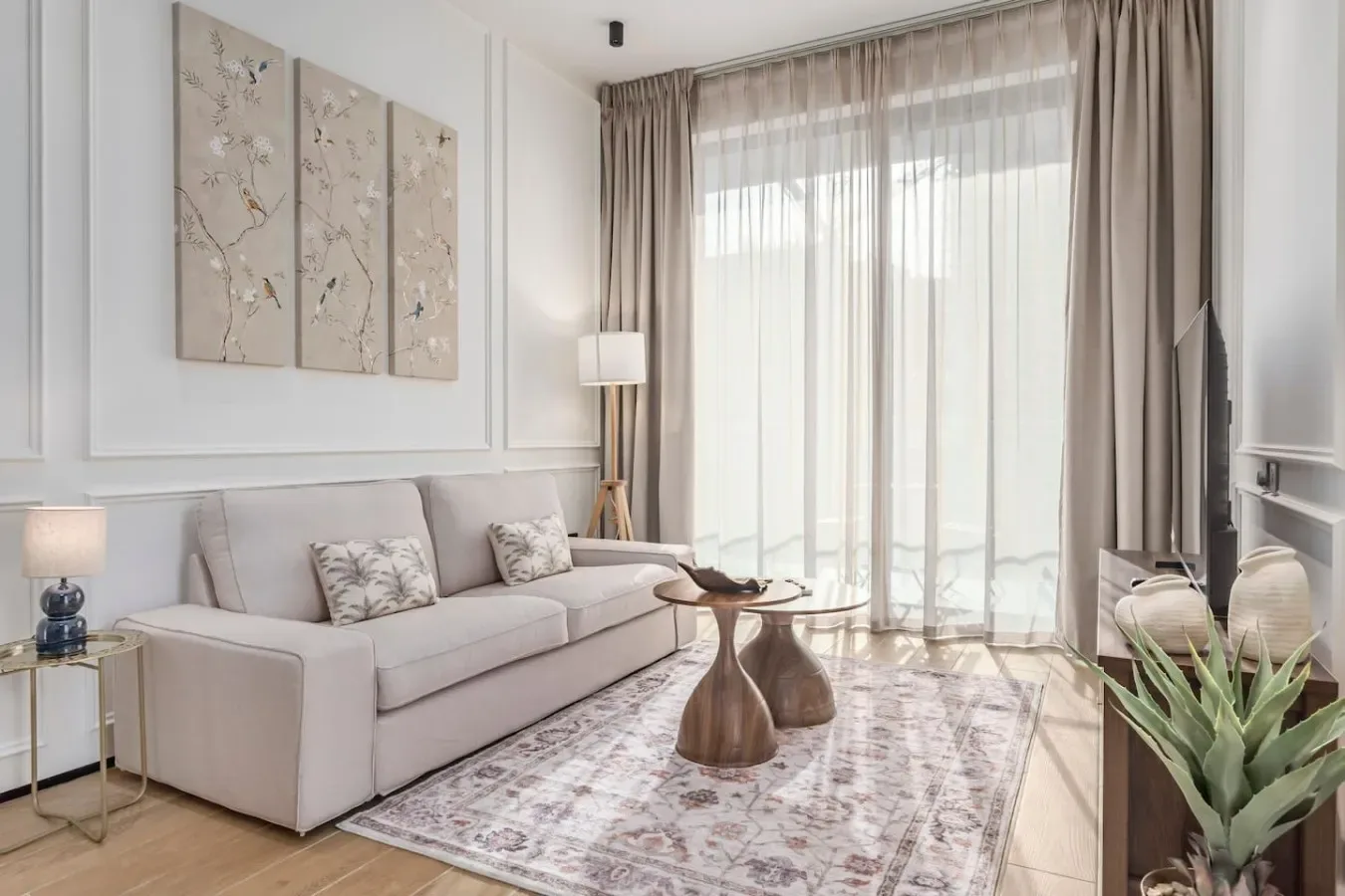 Una sala luminosa con sofá, mesa de centro y una gran ventana con cortinas.