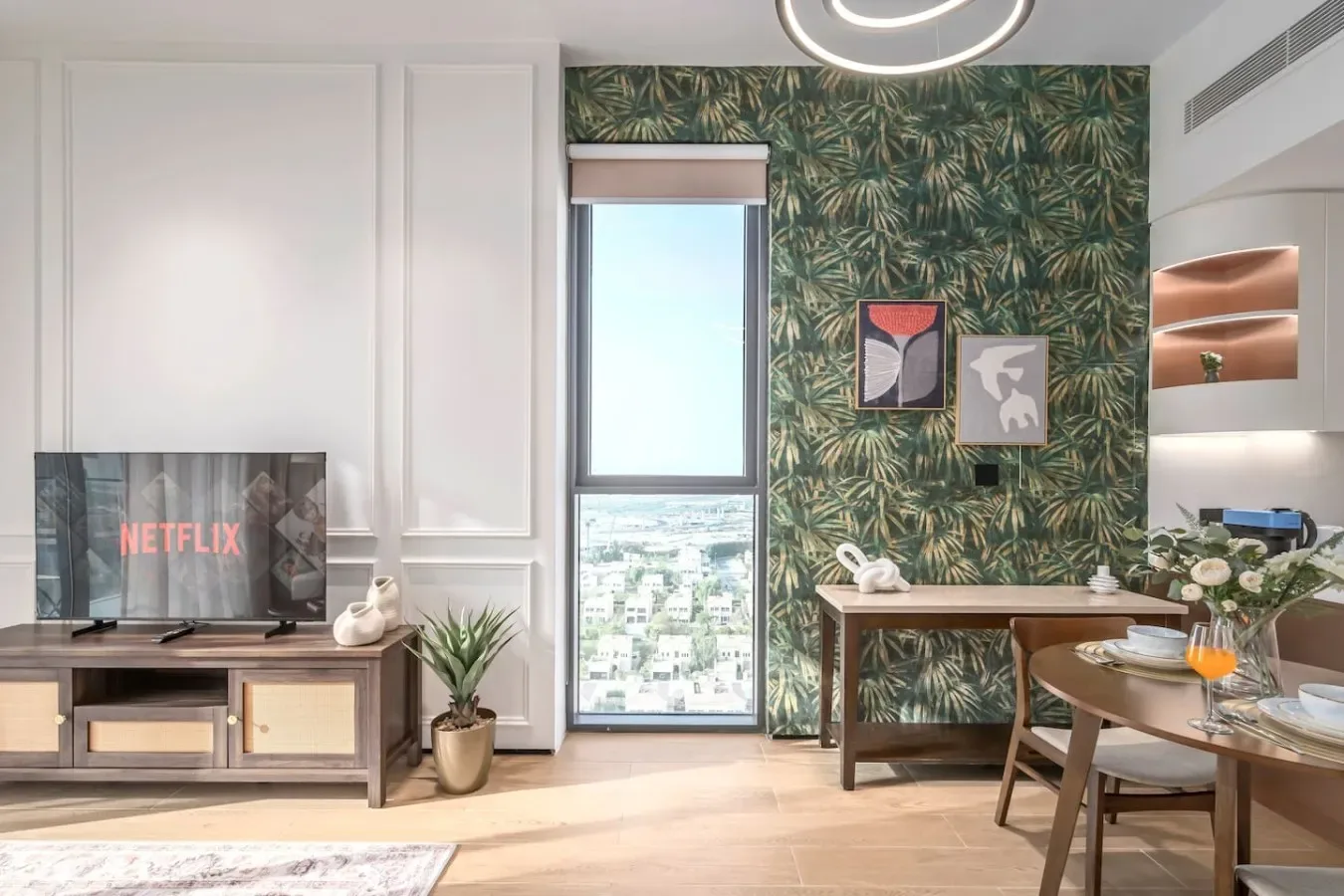 Una luminosa sala de estar y comedor con televisor, mesa y pared decorativa de hojas.