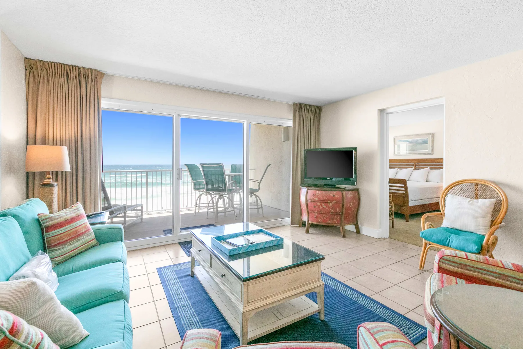 A bright living room opens onto a balcony with a view of the water.