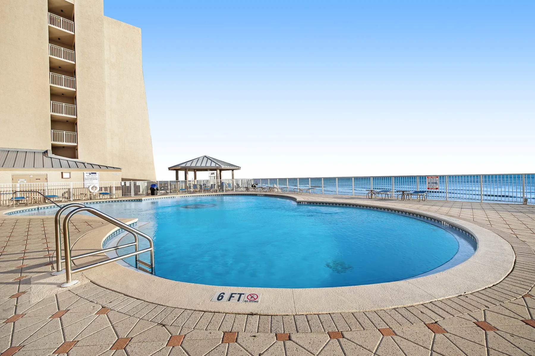 Una piscina al aire libre junto a una terraza frente al agua y un edificio alto.