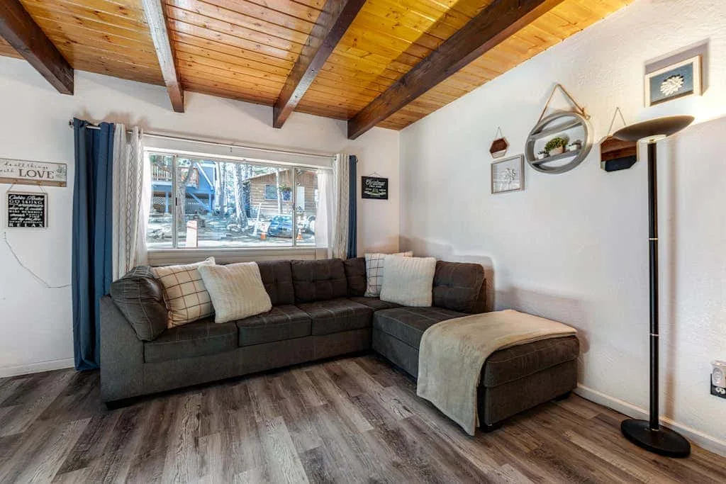 Living room with a dark sectional sofa beneath a wood-paneled ceiling.