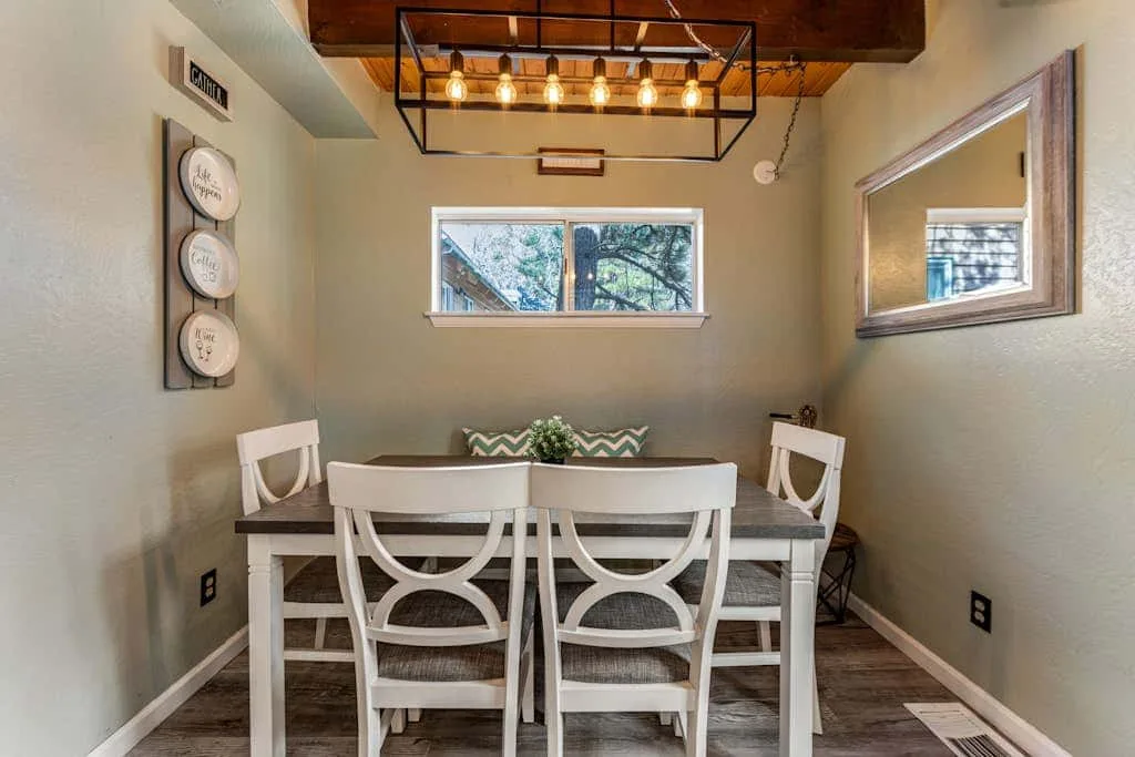 A dining area with a table and white chairs beneath a row of hanging lights.