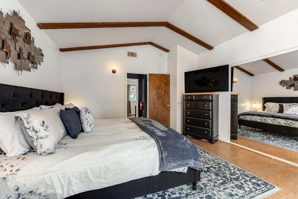 Un dormitorio con una cama, una cómoda oscura y un espejo grande.