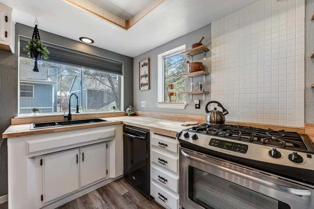 Una cocina luminosa con gabinetes blancos, una ventana grande y una estufa de gas.