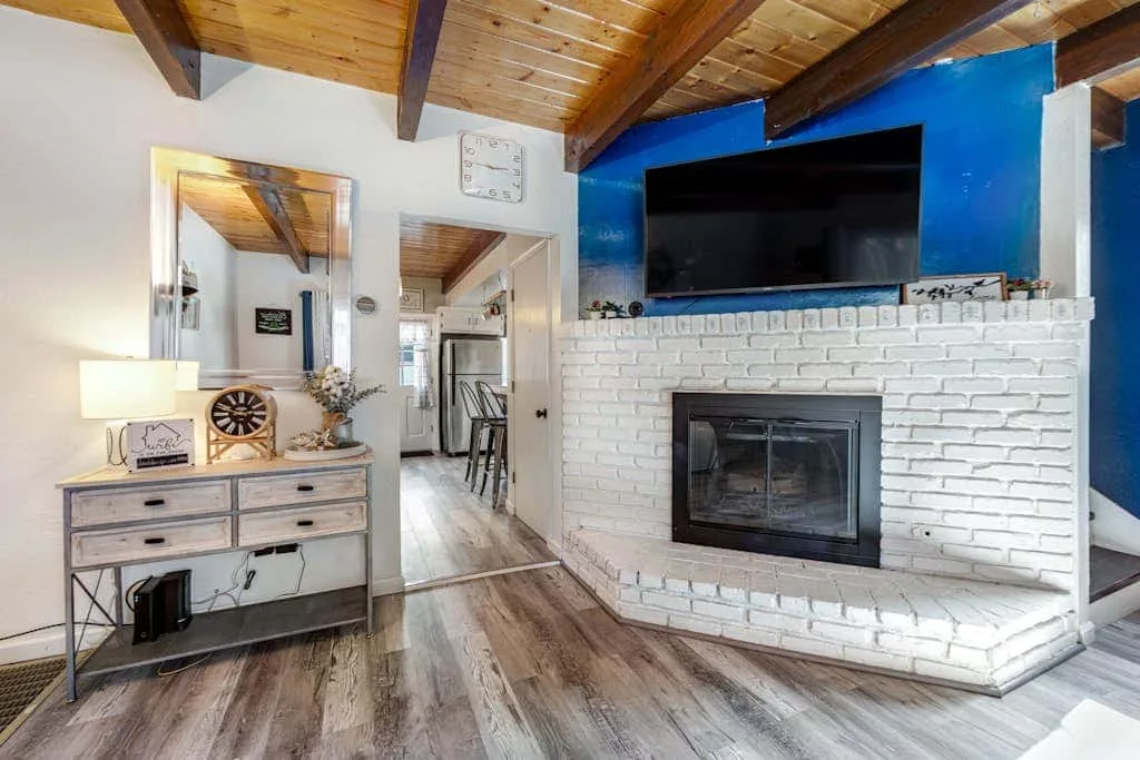 Sala de estar con chimenea de ladrillo blanco y televisor frente a una pared azul.