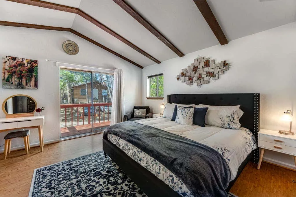 A bedroom with a large bed, a patterned rug, and a sliding glass door.