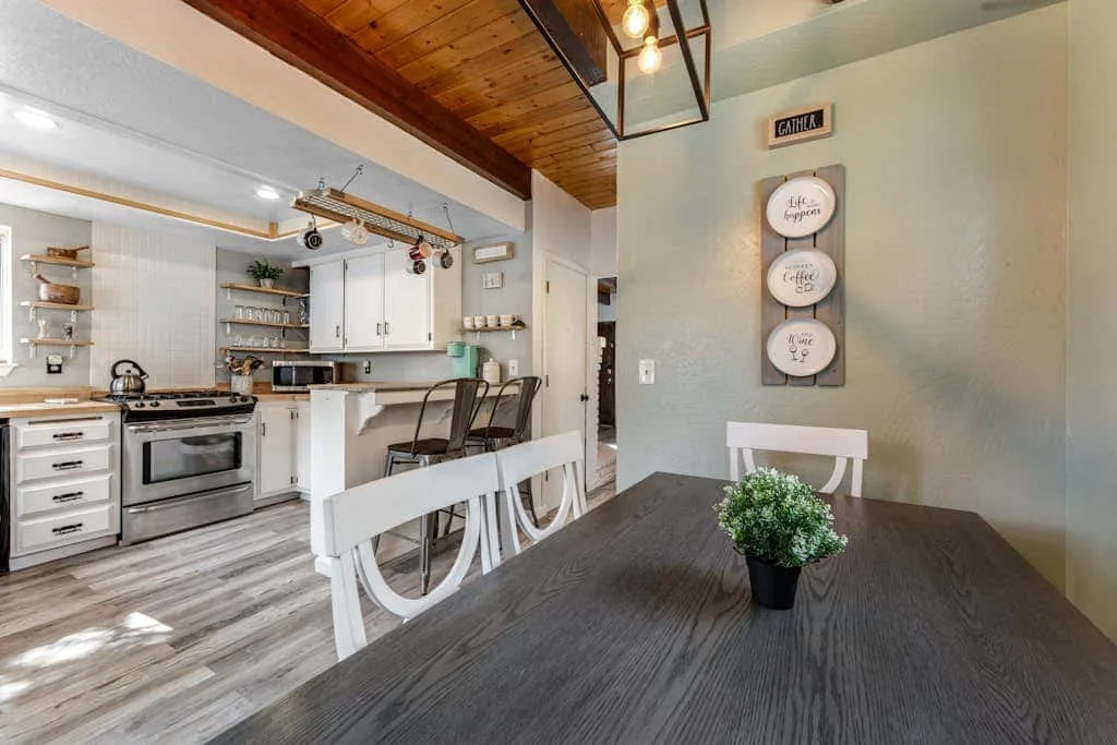 Cocina abierta y comedor con una mesa oscura y asientos blancos.