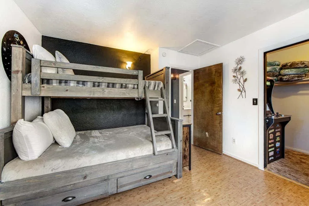 Un dormitorio con una litera gris y una cama inferior, junto a una puerta abierta.