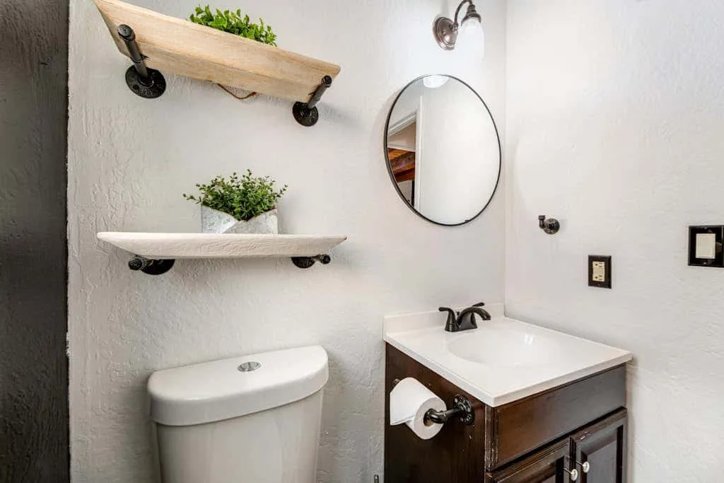 Un baño con lavabo, inodoro y espejo redondo en la pared.