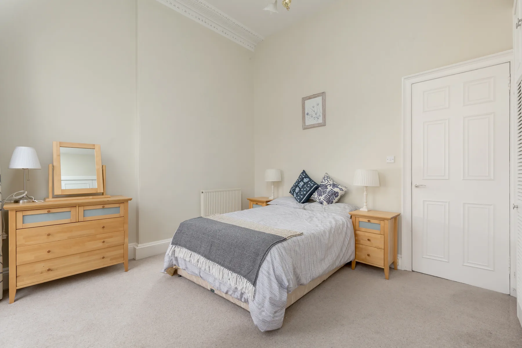 A bedroom with a double bed, wooden bedside tables, and a chest of drawers.