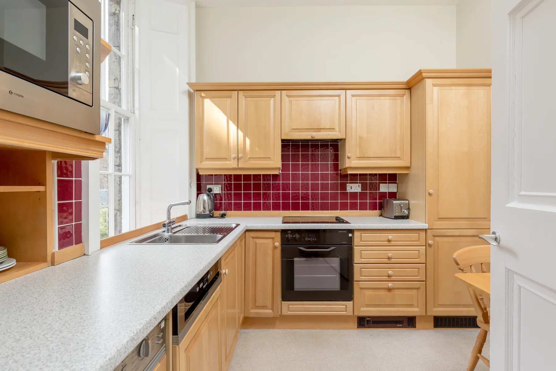 Una cocina luminosa con armarios de madera y un salpicadero de azulejos rojos.