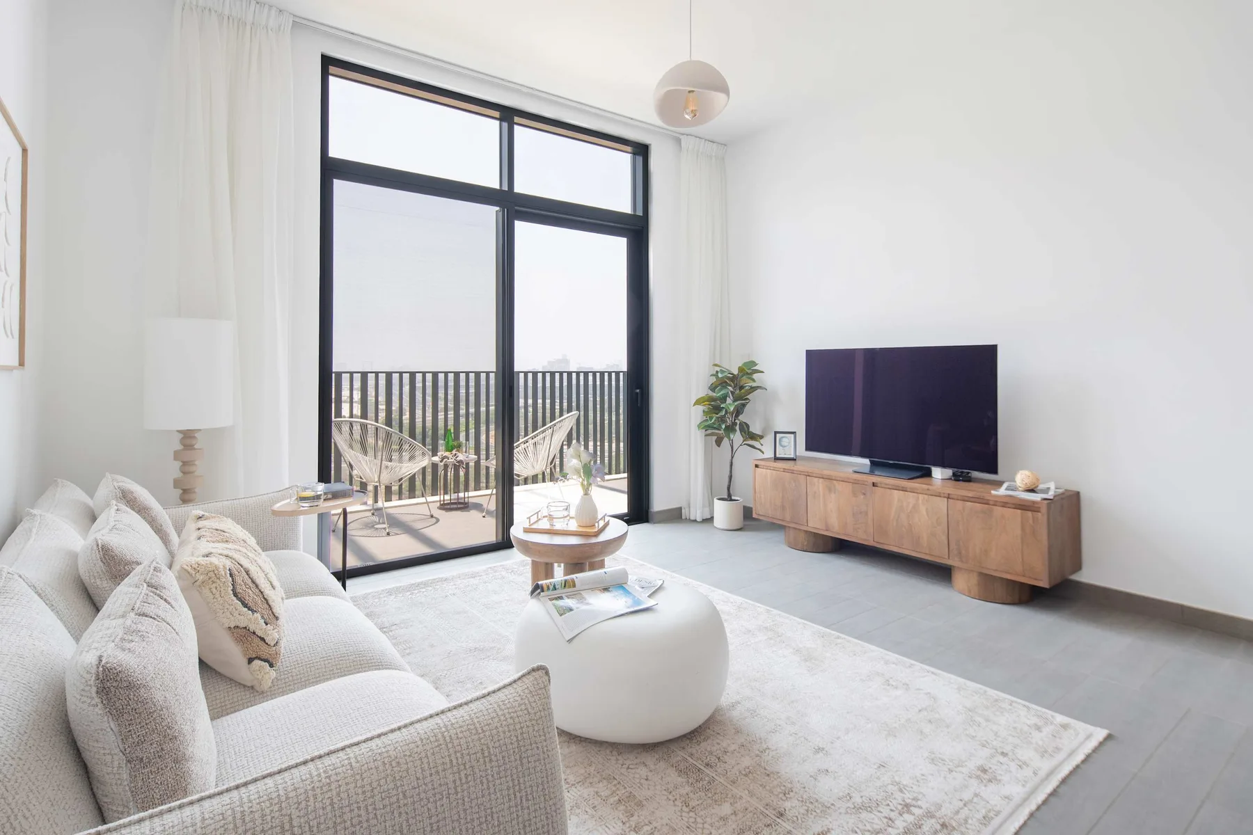 Sala de estar luminosa con sofá y televisor frente a una gran ventana.