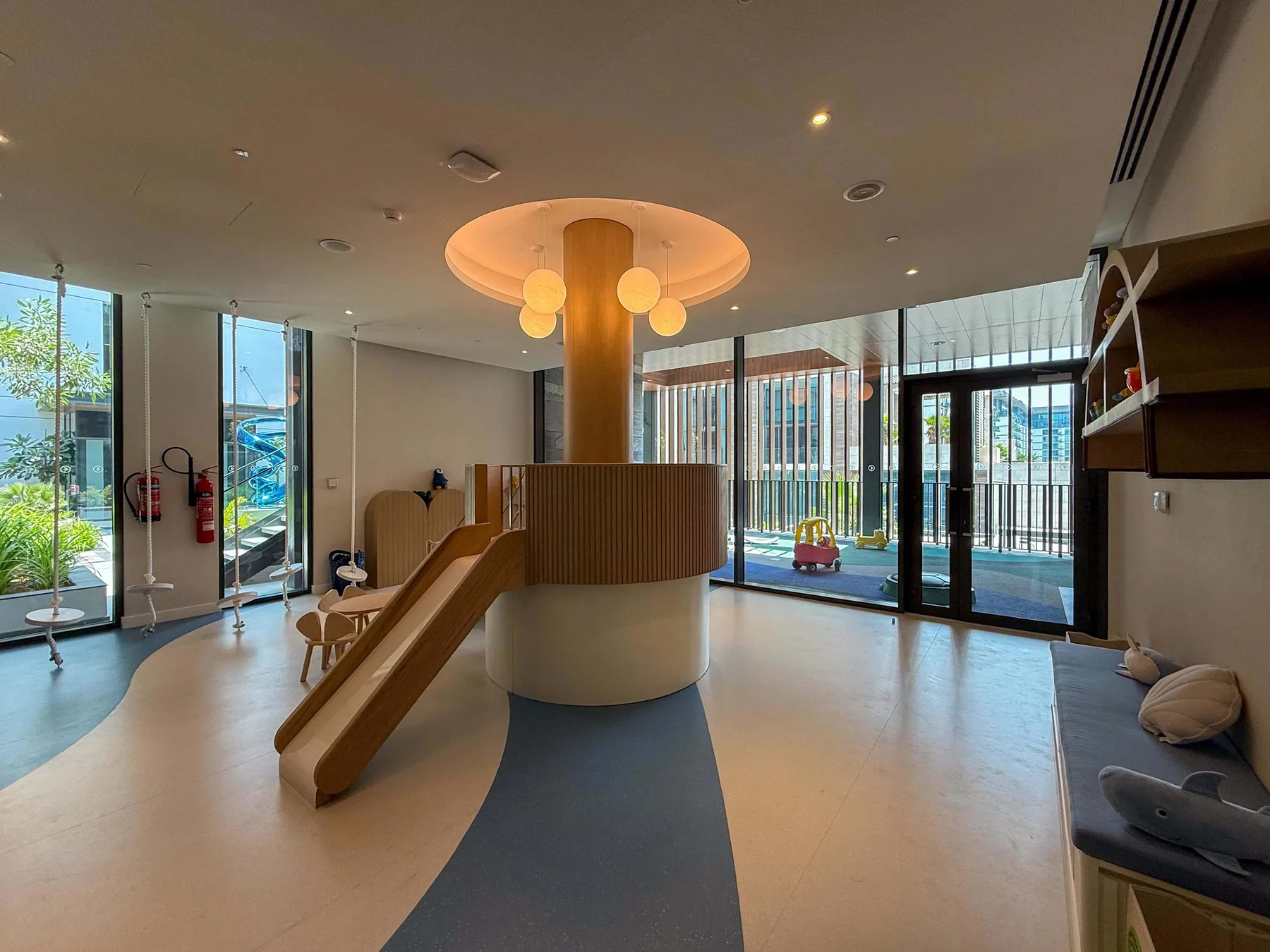 Un salón luminoso con un tobogán curvo de madera junto a ventanales.