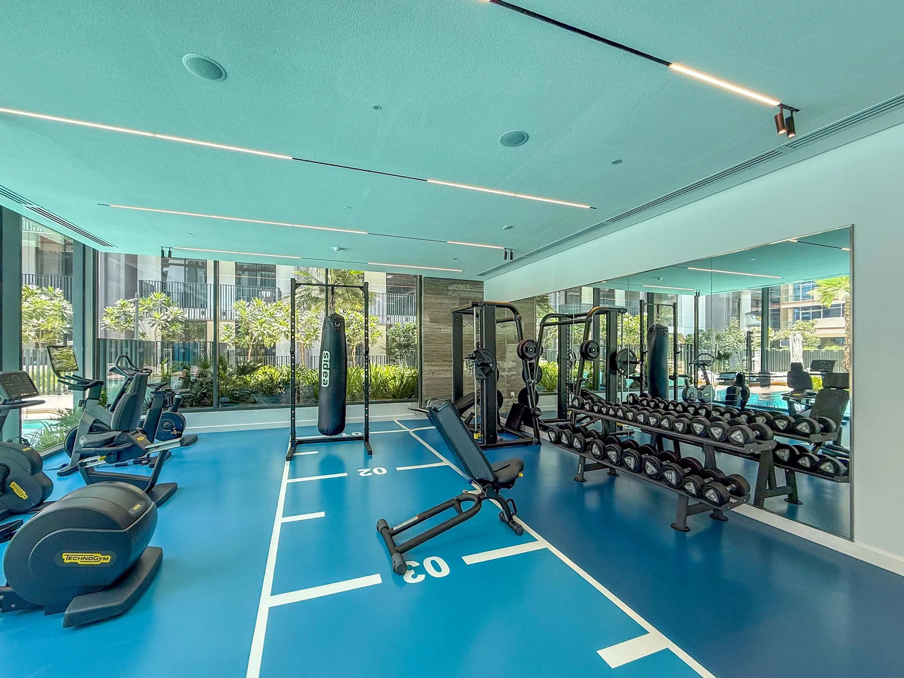 Un gimnasio con máquinas de ejercicio y pesas junto a grandes ventanales.