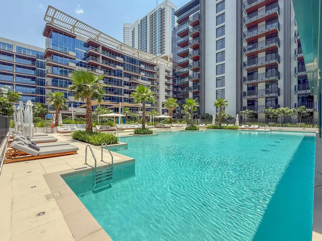 Una piscina está junto a edificios de apartamentos modernos y jardines.