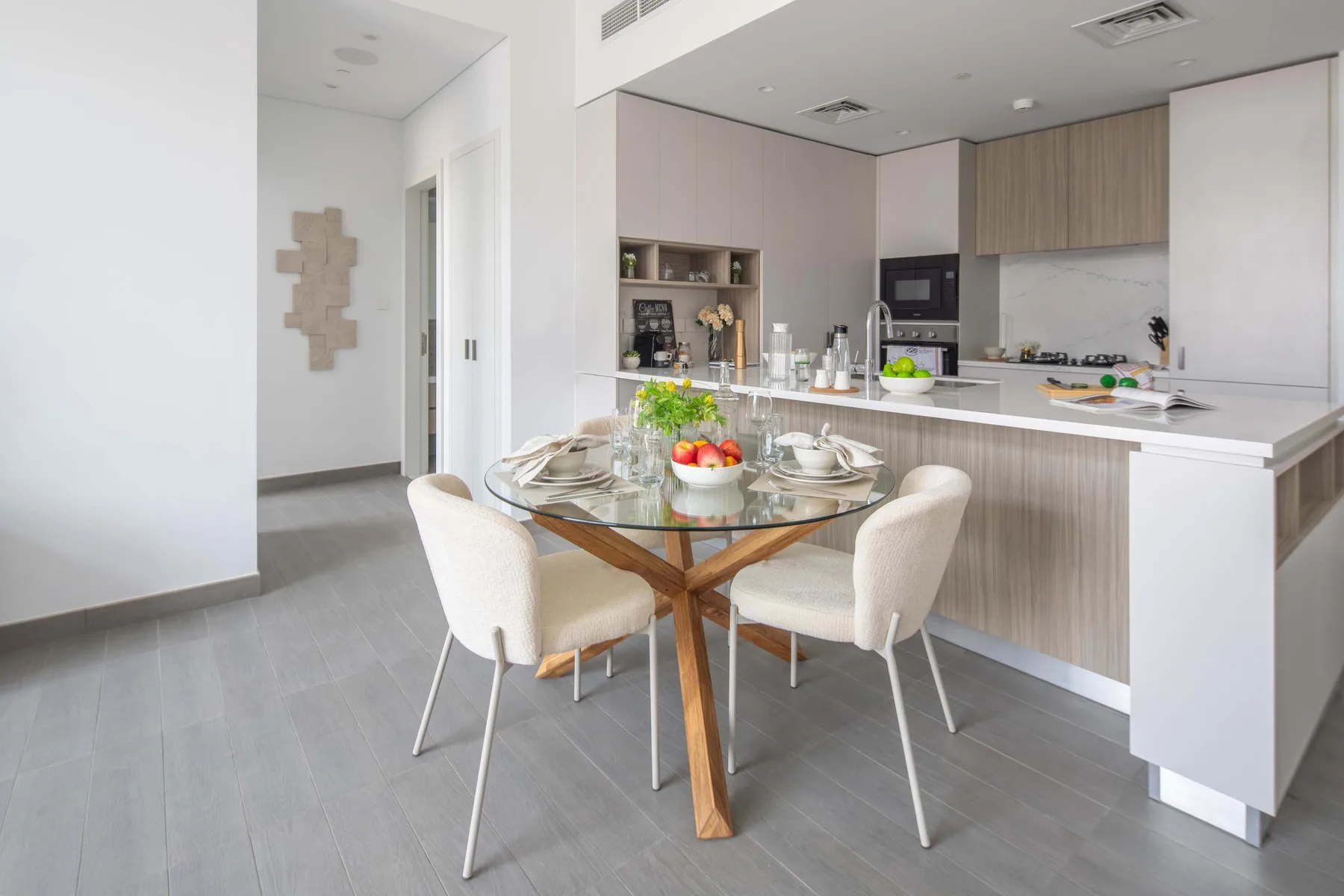 Un comedor luminoso junto a una cocina moderna, con una mesa de vidrio preparada para comer.