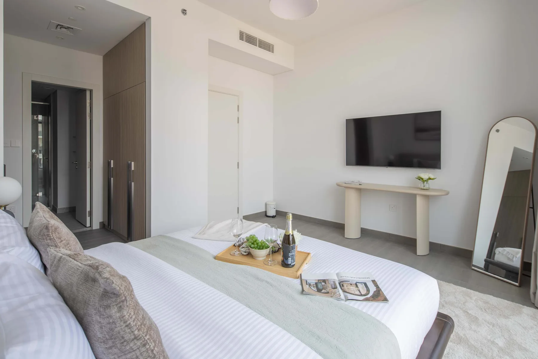 Un dormitorio luminoso con una cama bien arreglada y un televisor en la pared.