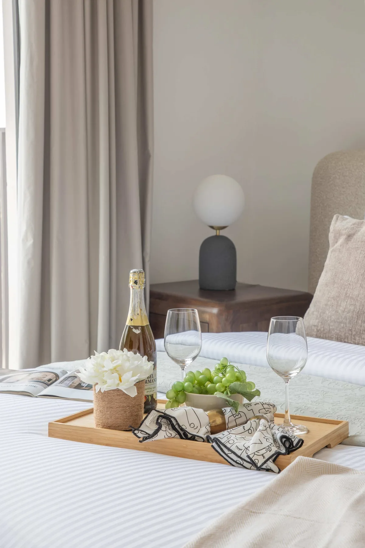 Un dormitorio ordenado con una bandeja de desayuno sobre la cama junto a la ventana.