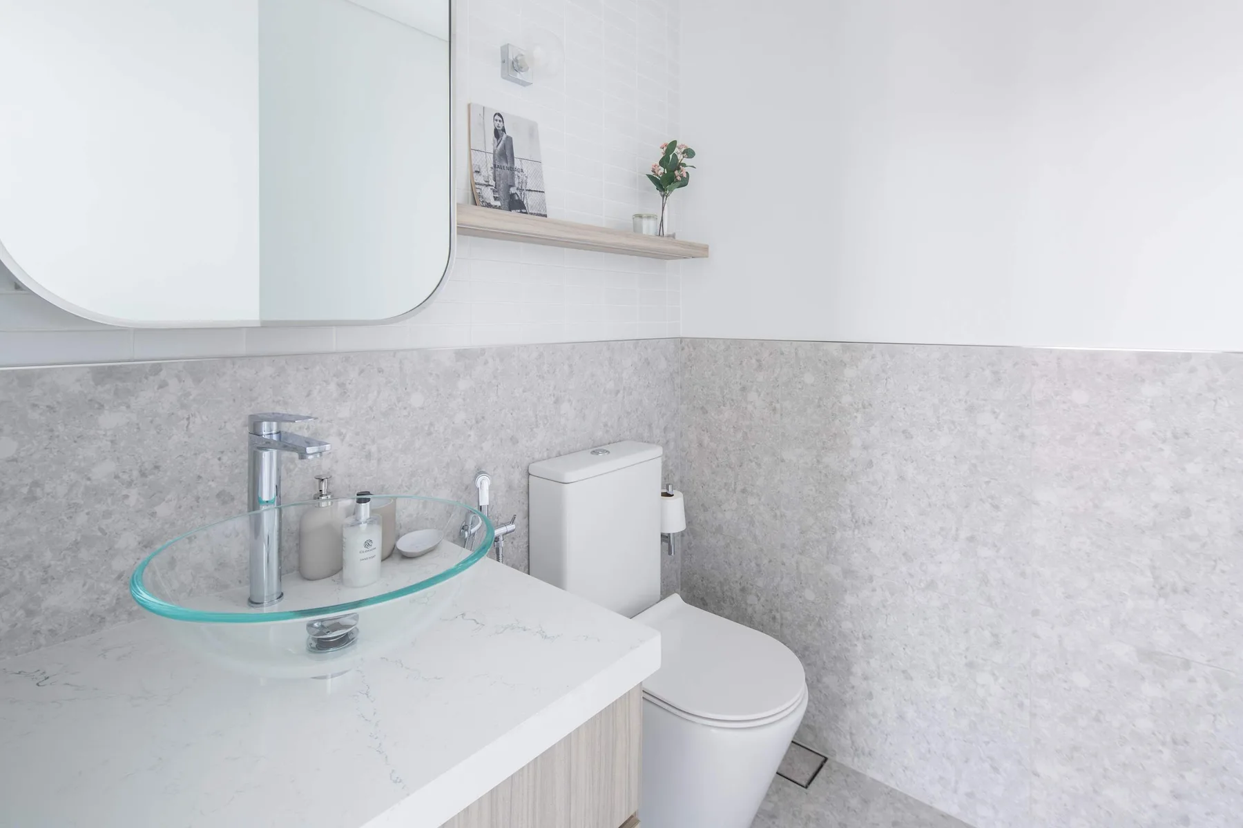 Un baño luminoso con un lavabo de vidrio y un inodoro junto al tocador.