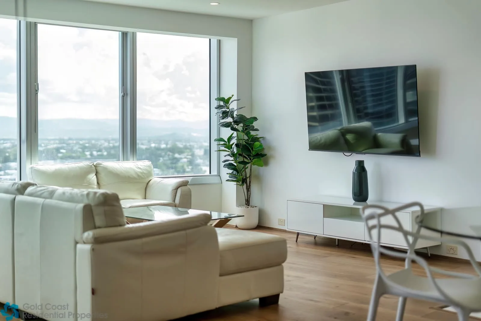 Una sala de estar con asientos, un televisor en la pared y ventanas grandes.