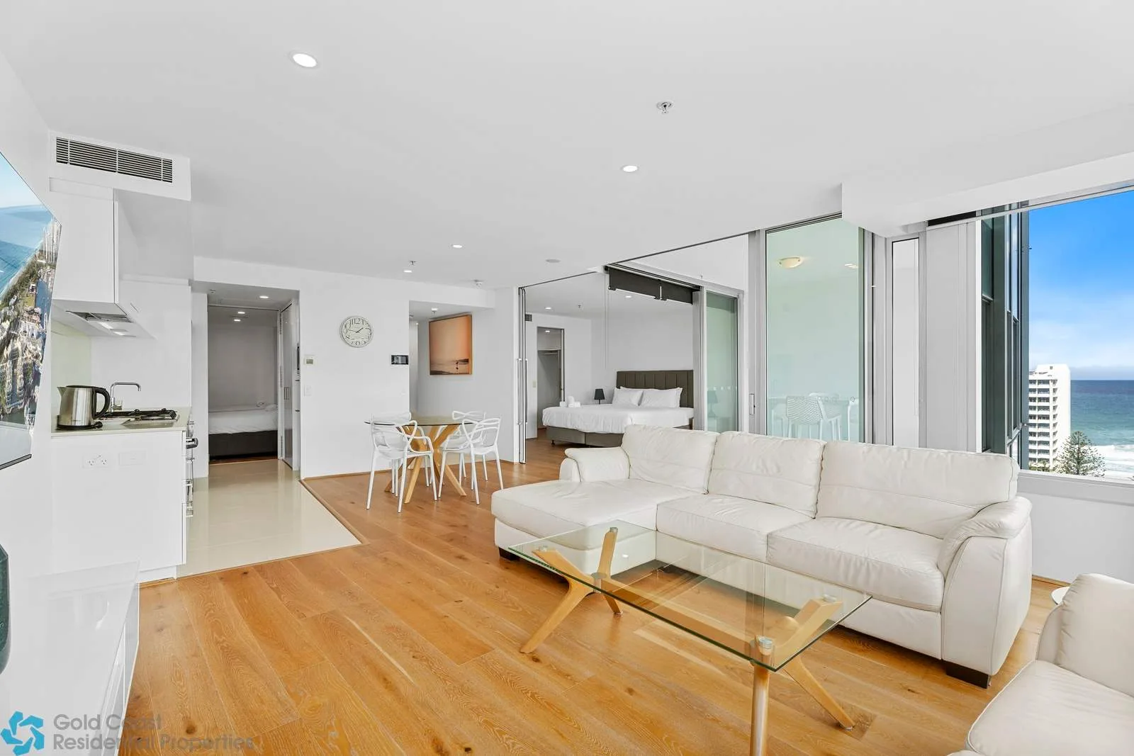 Una sala-comedor de planta abierta con un sofá seccional blanco y una mesa de centro de vidrio.
