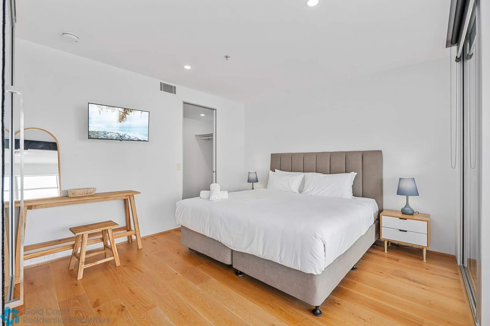 A bright bedroom with a large bed, bedside tables, and a wooden desk.