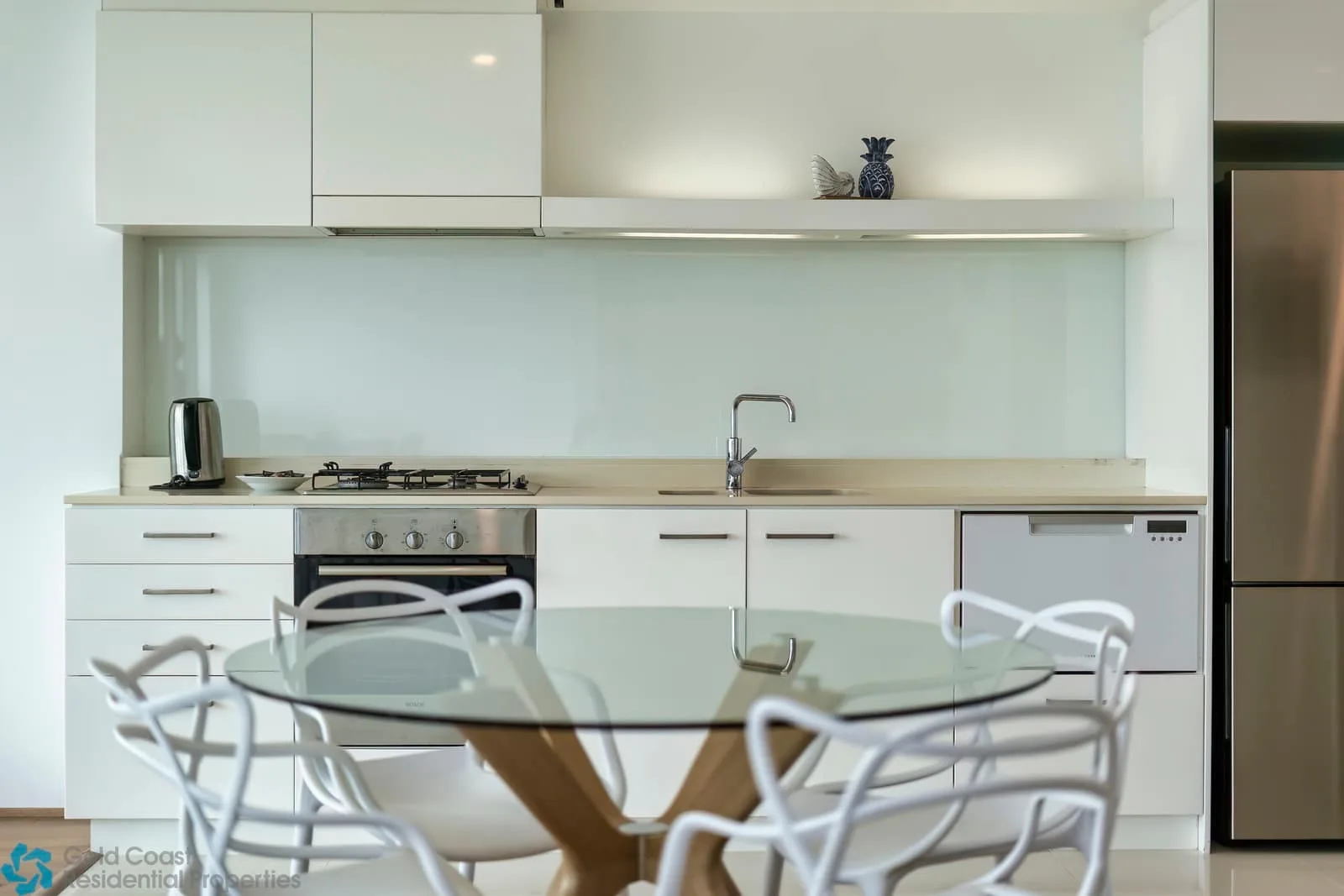 Una cocina moderna con una mesa de comedor de vidrio y asientos blancos.
