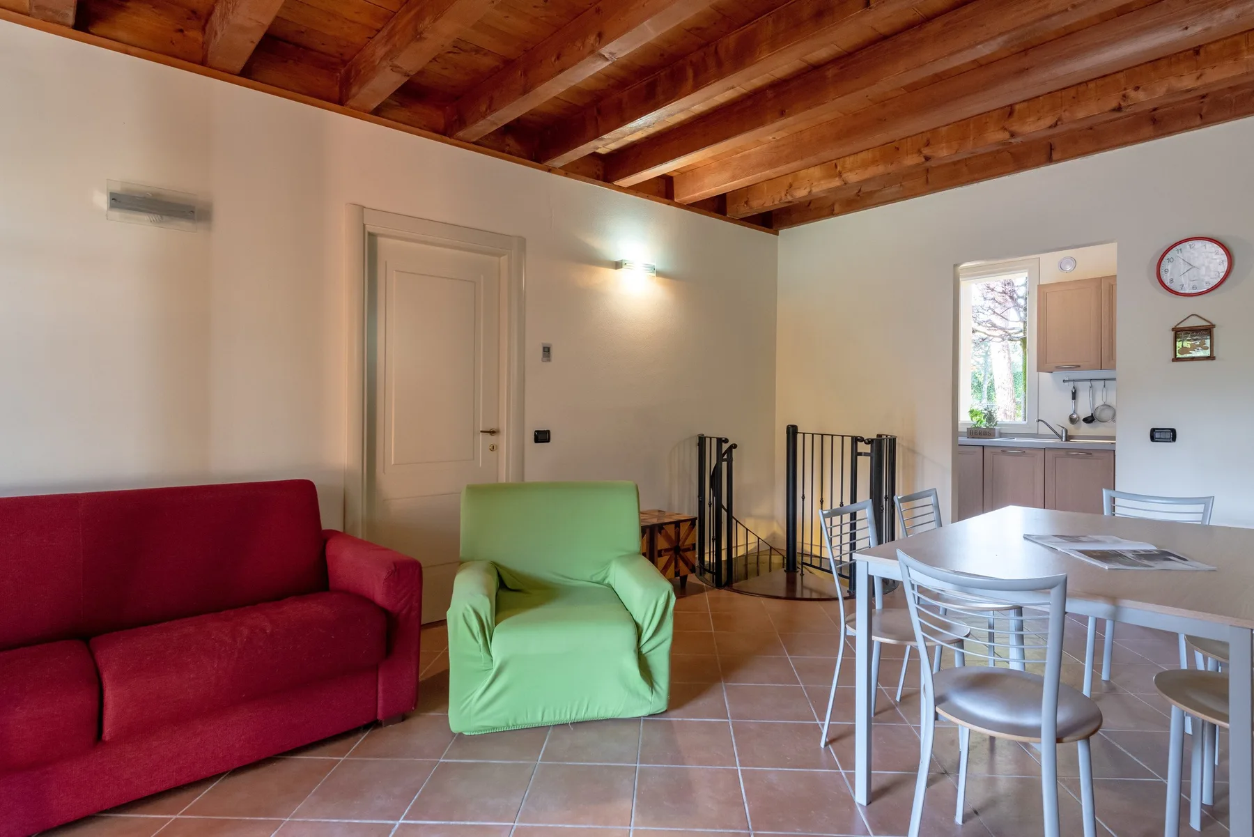 A living and dining area with colorful seating, a table, and a kitchen in the background.