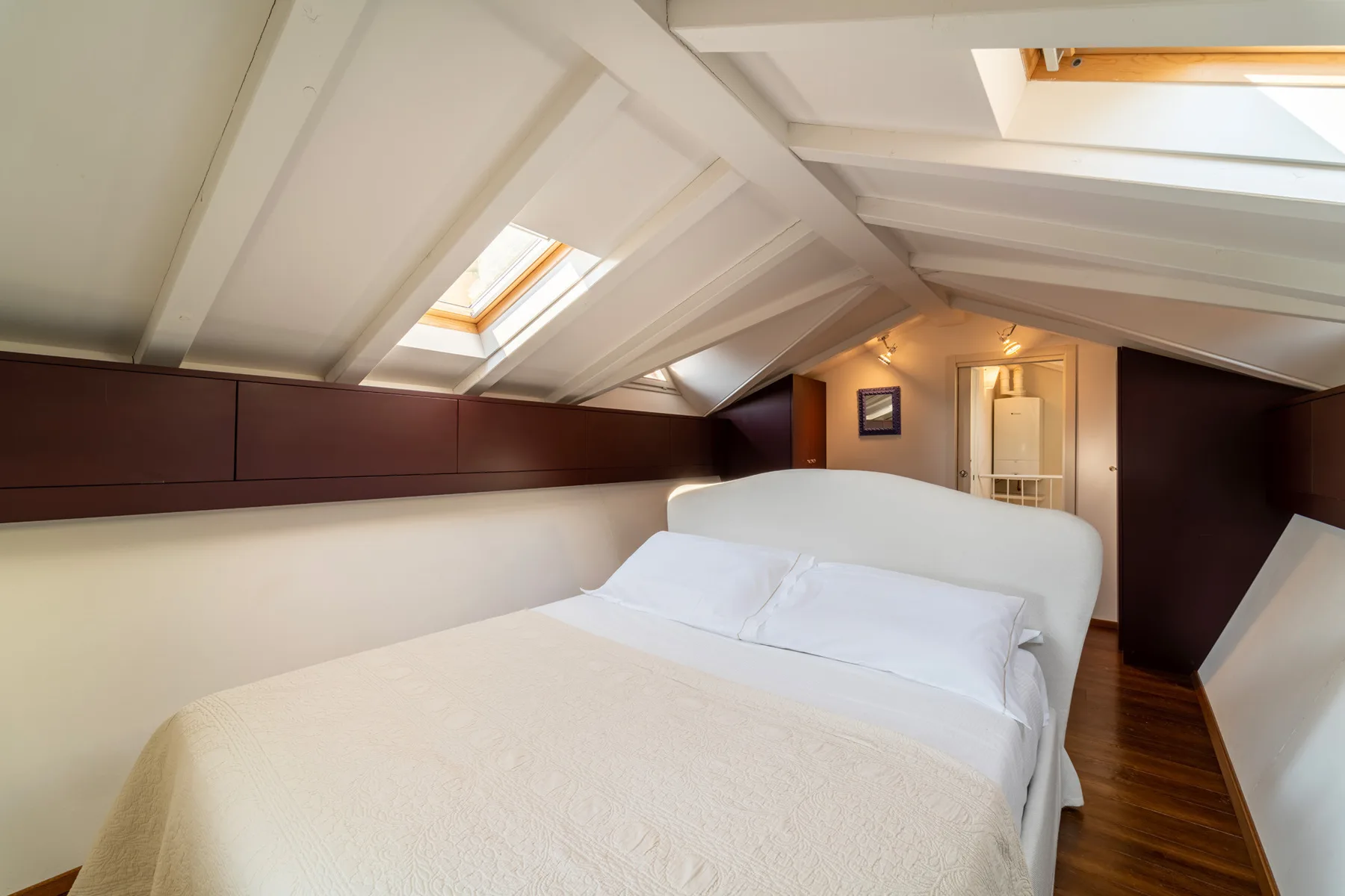 Un dormitorio con una cama bajo un techo inclinado y tragaluces.