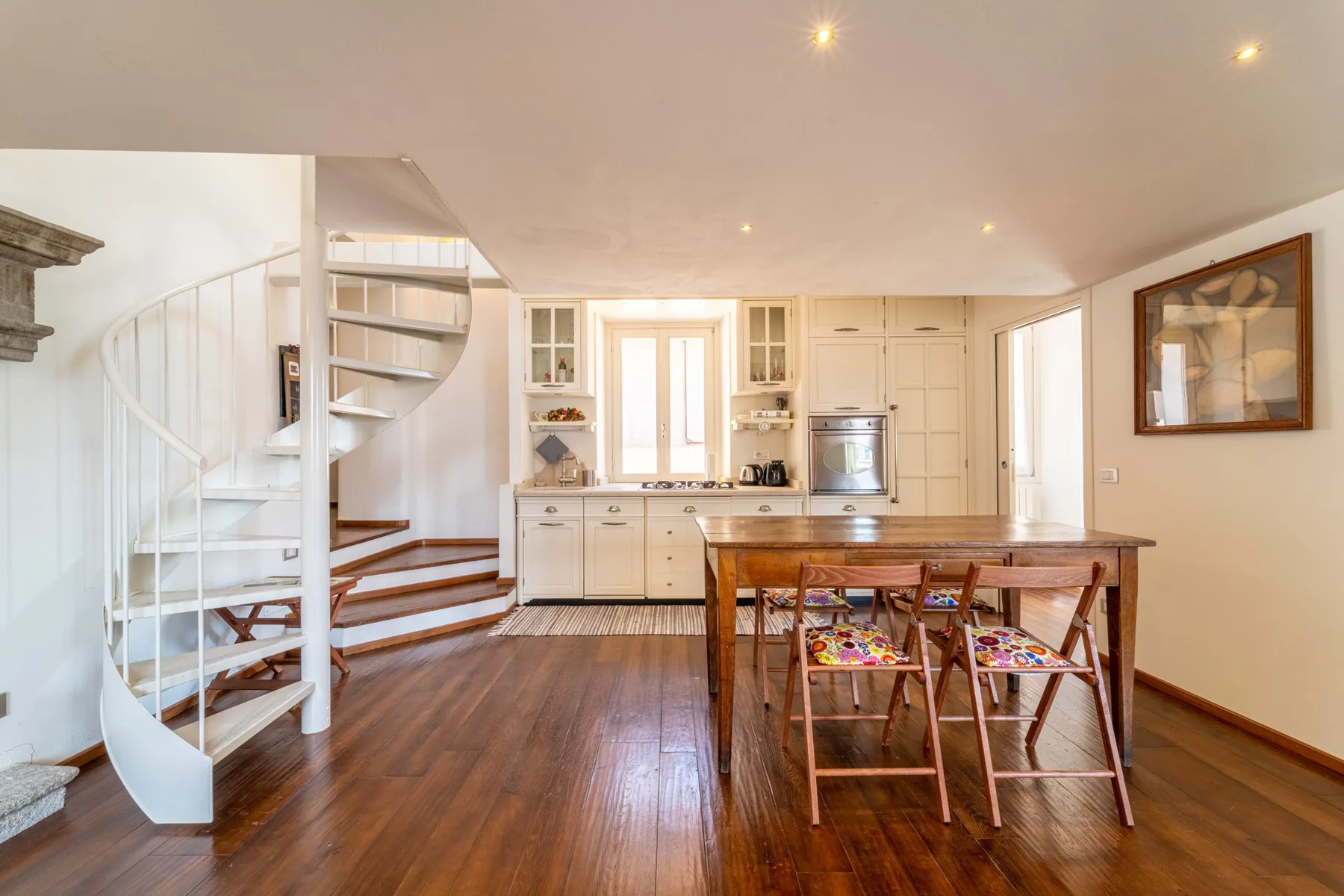 Una luminosa cocina y comedor con una escalera de caracol y una mesa de madera.